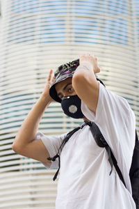 Man wearing a protective face mask to avoid corona virus infection while adjusting his bucket cap.