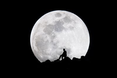 Silhouette of person sitting on mountain against moon at night