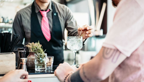 Midsection of bartender serving drink to man in bar