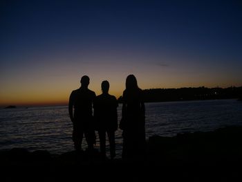 Silhouette of people standing by river at sunset