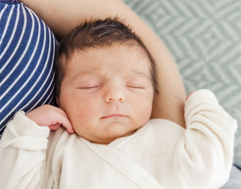 Cute baby boy sleeping on mother lap at home