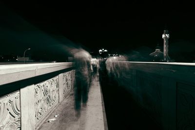 Blurred motion of people on footpath against sky at night