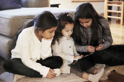 Sisters watching digital tablet while sitting on carpet at home