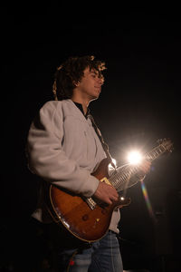 Man playing guitar against black background