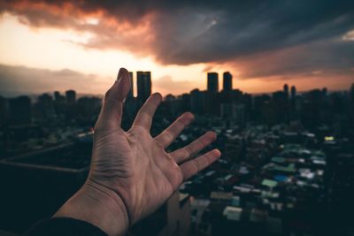 Close-up of human hand against sky during sunset