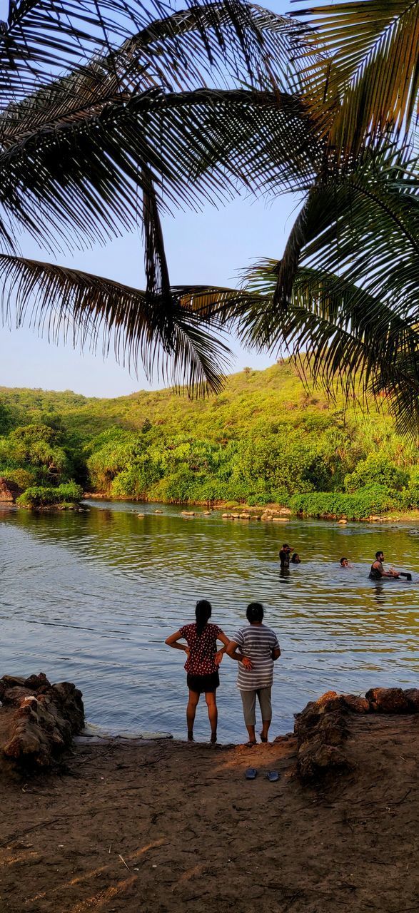 REAR VIEW OF PEOPLE STANDING AT BEACH