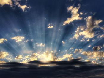 Low angle view of sunlight streaming through clouds