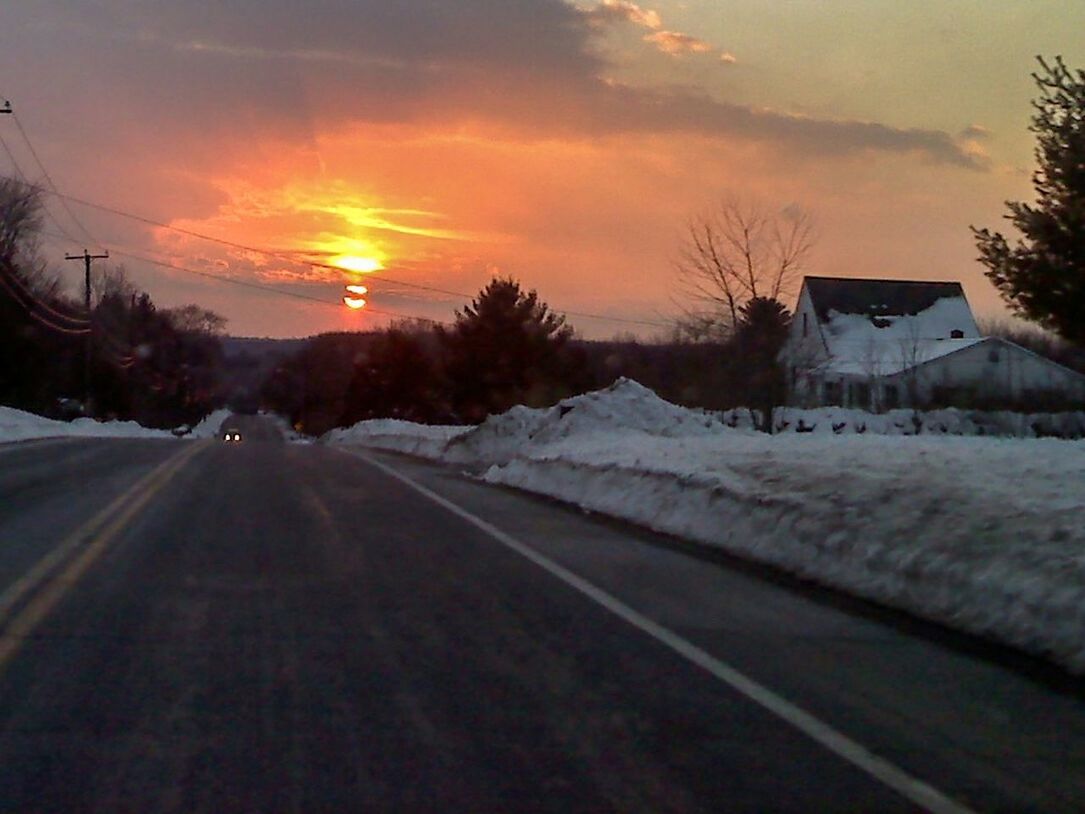 SNOW COVERED ROAD BY TREES AGAINST SKY DURING SUNSET