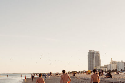 Rear view of shirtless men on beach against sky