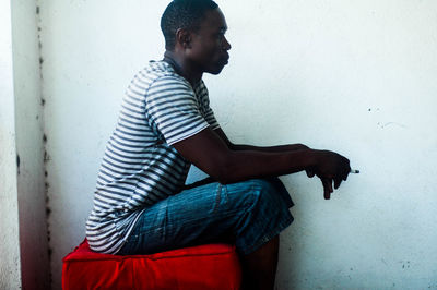 Side view of man sitting by wall