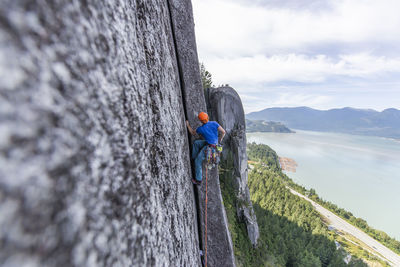 Side view of man climbing multi pitch route on pillar with ocean view