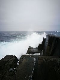 Waves splashing on rocks by sea against sky