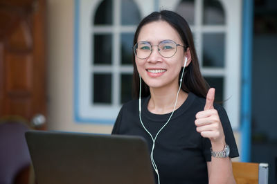 Portrait of smiling young woman gesturing while using laptop