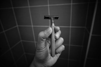 Cropped hand of man holding razor against wall