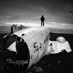 Rear view of man standing on wrecked airplane on landscape