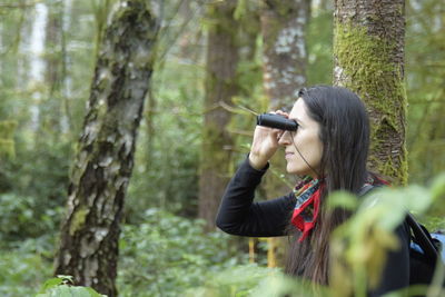 Woman photographing by tree trunk in forest