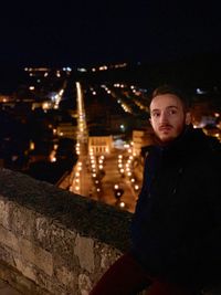 Portrait of young man sitting in city at night