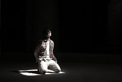 Light falling on man kneeling on floor against black background