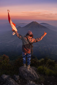 Rear view of person standing on rock against sky