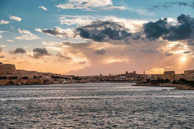 Scenic view of sea by buildings against sky during sunset