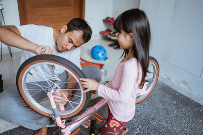 Father repairing bicycle with daughter at home