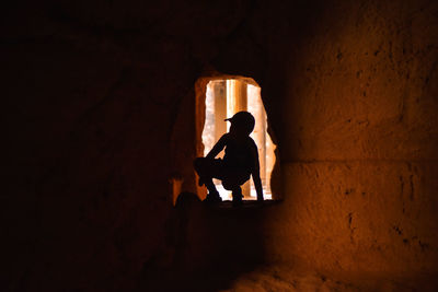 Silhouette boy crouching amidst rock formation