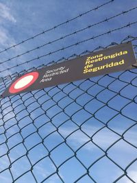 Low angle view of text on chainlink fence against sky