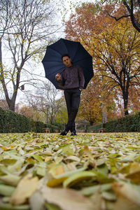 Portrait of man standing with umbrella on leaves covered park during autumn