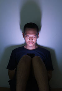 Portrait of young man sitting against wall at home