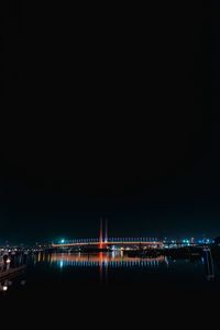 Illuminated city by river against sky at night