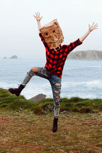 Person with paper bag on head jumping on shore