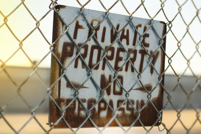 Close-up of text on chainlink fence against sky