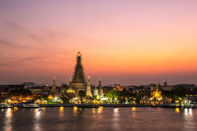 Illuminated buildings at waterfront during sunset