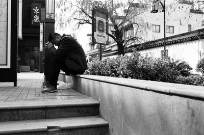 Side view of man sitting on staircase in city