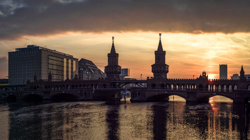 Bridge over river in city against cloudy sky