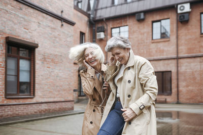 Cheerful female friends sharing headphones while listening music