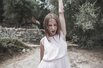 Portrait of teenage girl with mouth open standing against trees in park