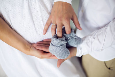 Hands of their parents, dressed in white, holding a knitted blue booties boy newborn