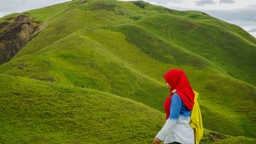 Woman walking on green hill against sky