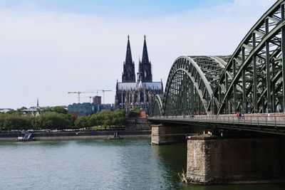 Bridge over river by buildings against sky