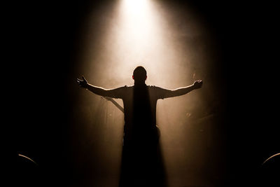 Rear view of silhouette man with arms outstretched during music concert