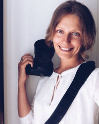 Portrait of smiling woman holding dslr against wall