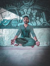 Full length of young man meditating while levitating against wall