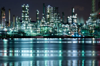 Illuminated factory by river against sky at night