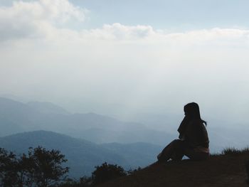 Woman sitting on mountain against sky during foggy weather
