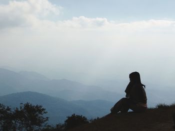 Woman sitting on mountain against sky during foggy weather