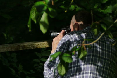 Rear view of senior man photographing in forest