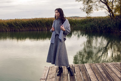 Woman stands next to the lake in a sweater and a scarf in the fall