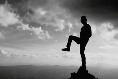 Silhouette man standing on cliff against sky