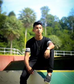 Young man looking away while sitting against trees